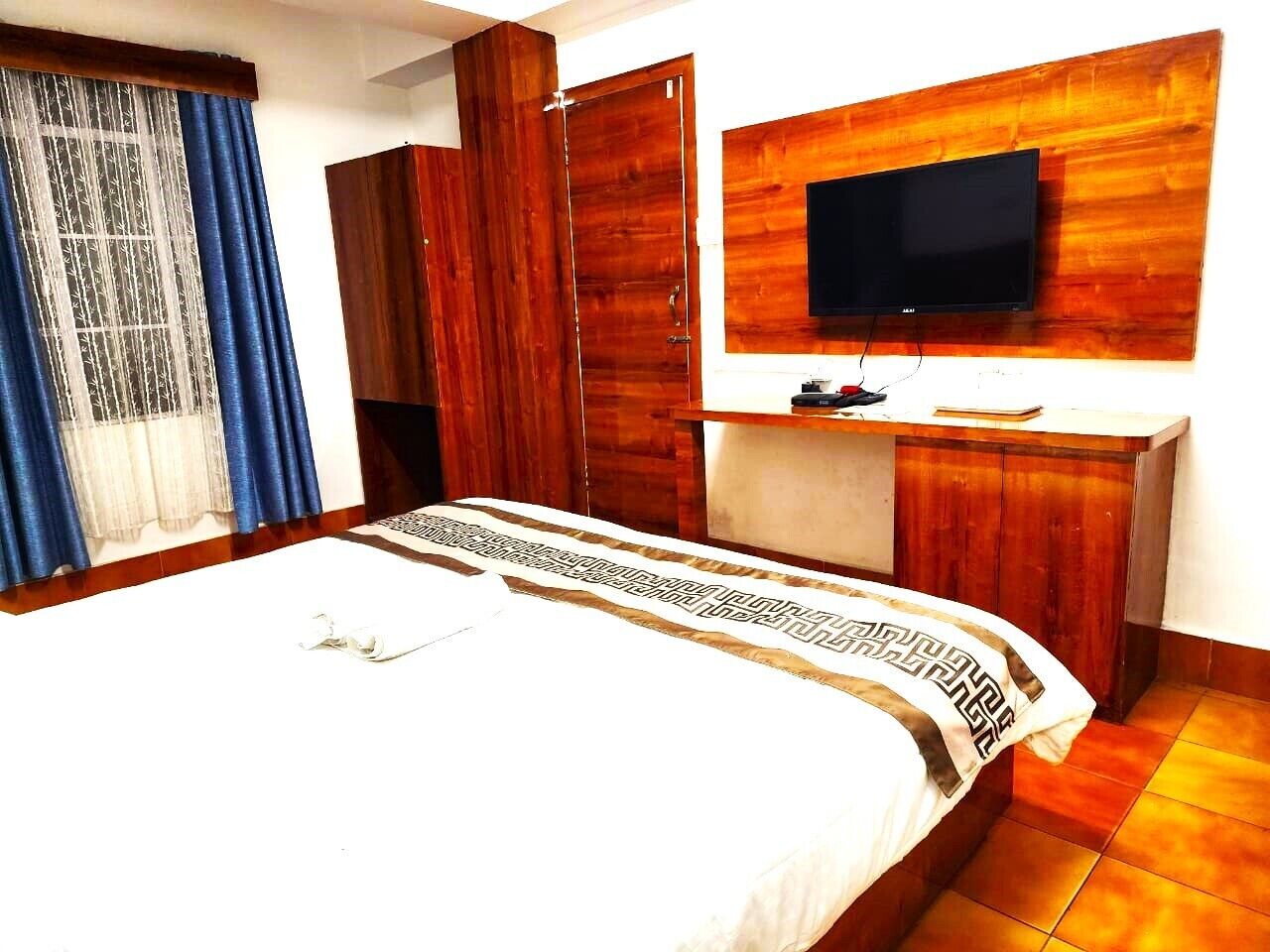Ein Hotelzimmer mit einem großen Bett, einem Holfischschrank, einem flachbildfernseher an der Wand und einem Schreibtisch mit Stuhl.