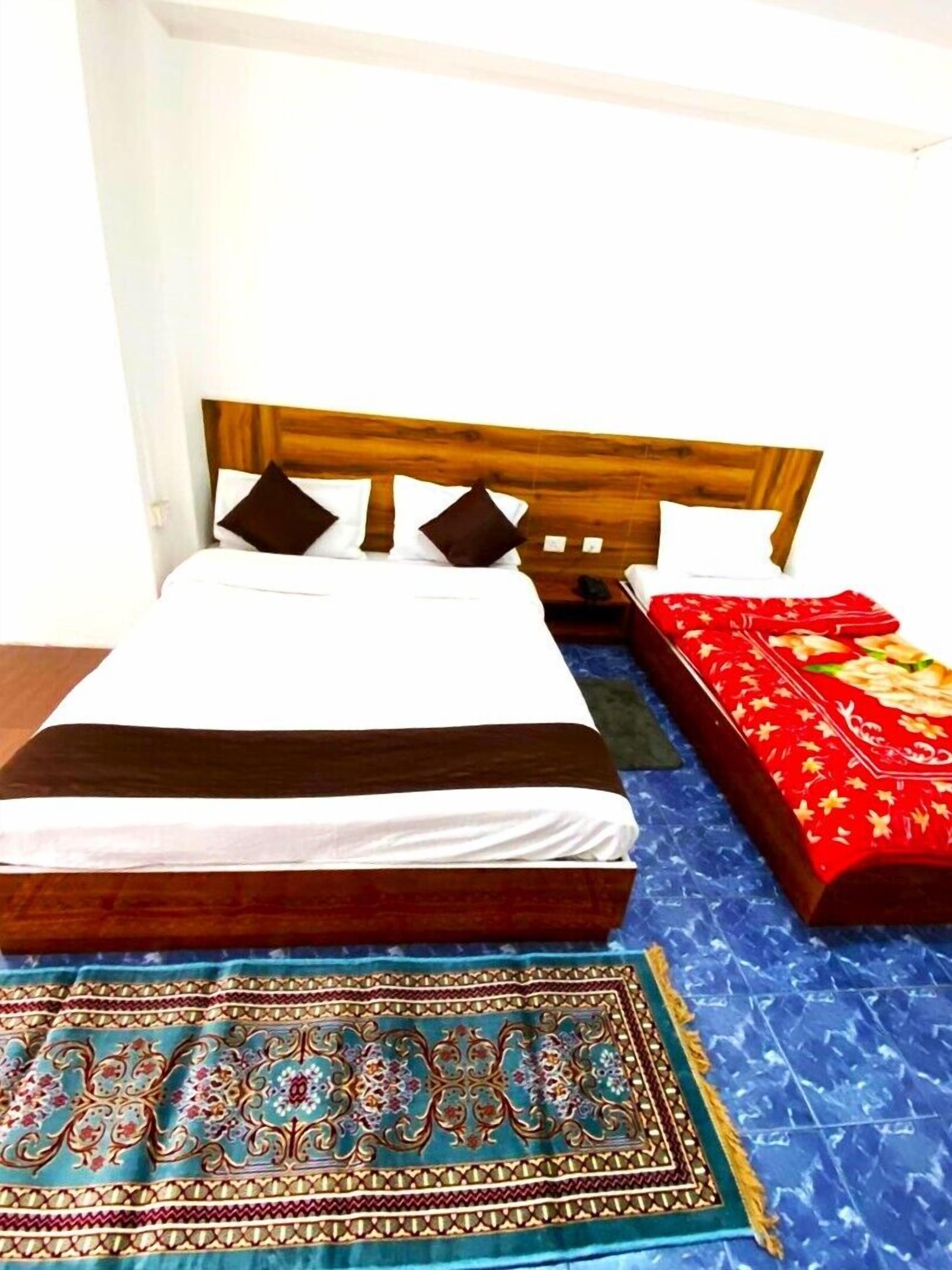 A bed with a wooden headboard, white bedding, and a red patterned blanket.