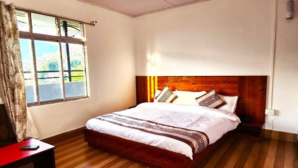 A bedroom with a wooden bed, a nightstand, a window with curtains, and a wooden floor. - HOTEL JADE ARITHANG GANGTOK (Gangtok)