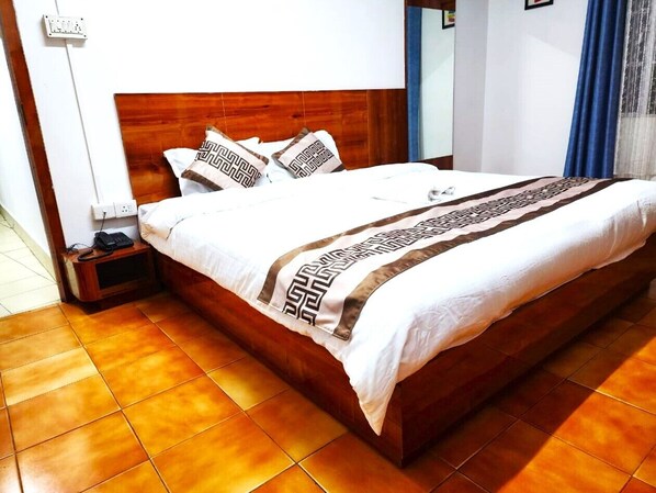 Cama bem arrumada com colcha estampada, cabeceira de madeira e mesa de cabeceira com um telefone.
