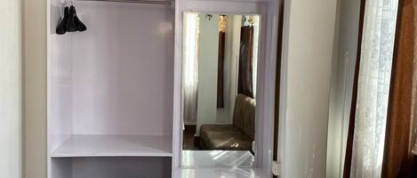 A room with a built-in wardrobe, a mirror, a brown sofa, and a wooden floor.