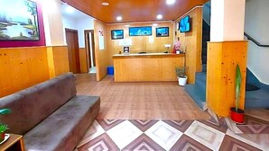 A reception area with a wooden reception desk, a sofa, and a patterned floor. - HOTEL JADE ARITHANG GANGTOK (Gangtok)
