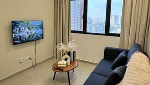 Un salon moderne doté d’un téléviseur à écran plat, d’un canapé, d’une table basse et offrant une vue sur de hauts immeubles à travers de grandes fenêtres.