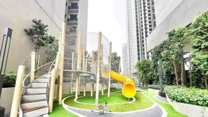 Un terrain de jeux doté d’un toboggan en spirale et d’une structure d’escalade, le tout entouré de gazon synthétique, avec en arrière-plan une rangée d’immeubles imposants.