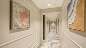 A hallway with marble flooring, framed artwork on the walls, and a ceiling with recessed lighting. - HOTEL GRAND SHIVA (Ahmedabad)