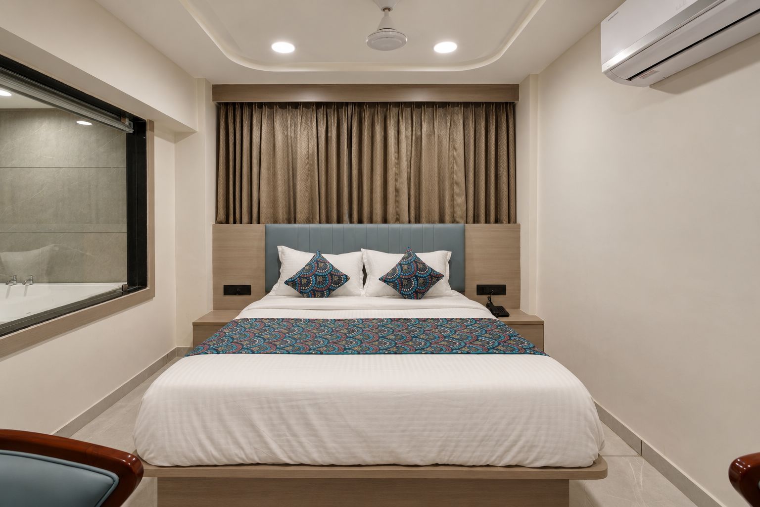 Habitación de hotel con cama, ventana, equipo de aire acondicionado y mesita de noche.