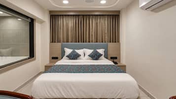 A hotel room with a bed, a window, an air conditioning unit, and a bedside table.
