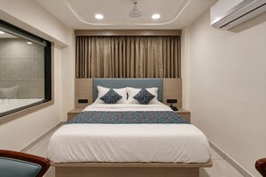 Een hotelkamer met een bed, een raam, een airconditioning en een nachtkastje.