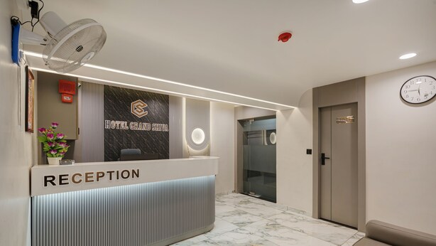 A hotel reception area with a marble floor, a reception desk, a clock, and a door. - HOTEL GRAND SHIVA (Ahmedabad)