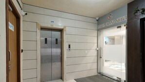 A hotel entrance with a modern design, featuring a large glass door, a wooden door, and a visible elevator. - HOTEL GRAND SHIVA (Ahmedabad)