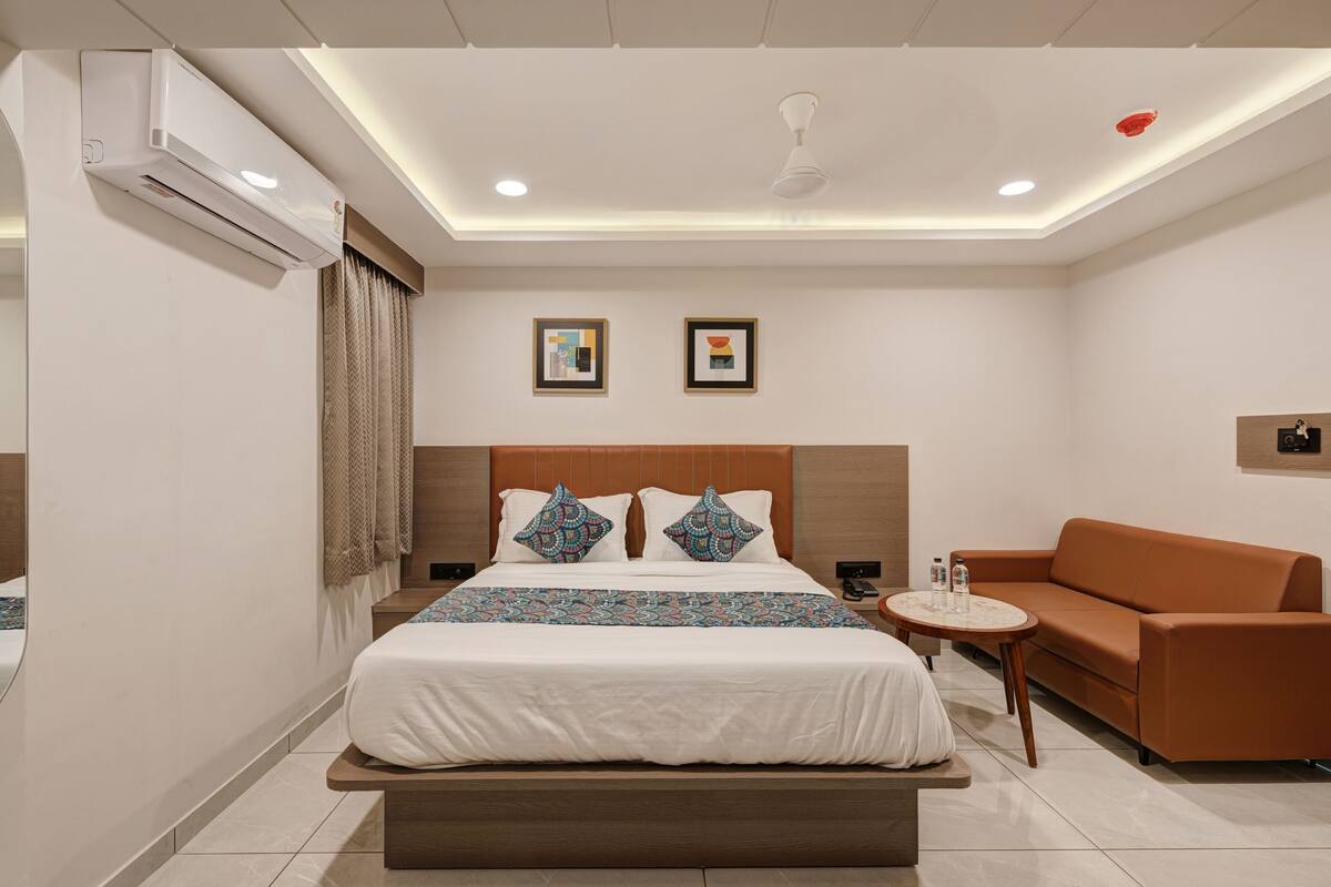 A modern hotel room with a large bed, a brown sofa, a small round table, and two framed pictures on the wall.