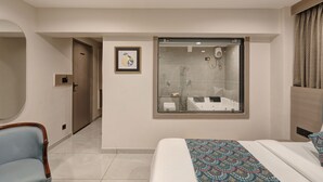 A modern hotel room with a large bed, a bathroom with a glass shower enclosure, and a door leading to another room. - HOTEL GRAND SHIVA (Ahmedabad)