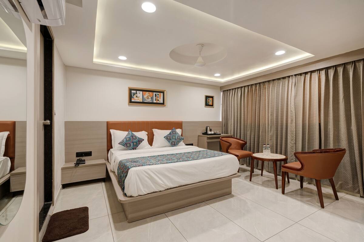 A modern hotel room with a large bed, a desk, two chairs, and a ceiling fan.