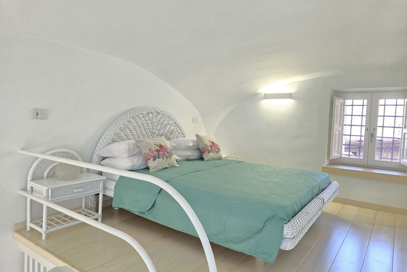A bedroom with a curved ceiling, a bed with a green bedspread, a wicker headboard, and a window with a view.