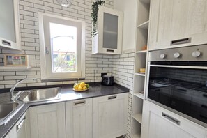 A kitchen with white cabinets, a black countertop, a sink, and an oven. - Grazy Home | Private Terrace, Summer Pool & Relaxation in Vico Equense (Vico Equense)