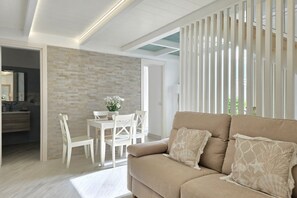 Ein modernes Wohnzimmer mit einem beigen Sofa, einem Esstisch mit Stühlen und einem durch einen offenen Durchgang einsehbarer Küchenbereich.