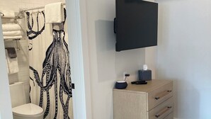 A modern bathroom with a toilet, shower curtain, and a mounted television. - Great Island Inn - Standard Queen Guest Room (New Castle)