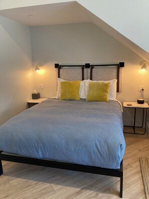 A bedroom with a bed, two bedside lamps, a nightstand, and a headboard. - Great Island Inn - Standard Queen Guest Room (New Castle)