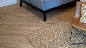 A bedroom with a bed, a map on the wall, a nightstand, and a chair. - Great Island Inn - Standard Queen Guest Room (New Castle)