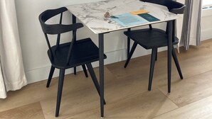 Une table à manger avec un plateau en marbre, deux chaises noires et une œuvre d’art représentant un cygne, encadrée, accrochée au mur.