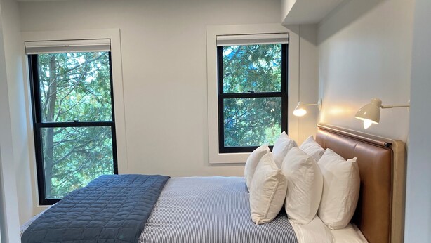 Une chambre à coucher avec un lit, deux fenêtres, une table de chevet et une lampe.