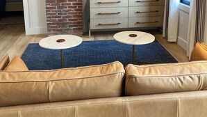 Un salon moderne avec un mur d’accent en briques, un téléviseur à écran plat, un canapé beige et deux tables rondes.
