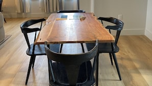 Un espace repas avec une table en bois et des chaises noires, un luminaire suspendu et une vue dégagée grâce à de grandes fenêtres ornées de rideaux.