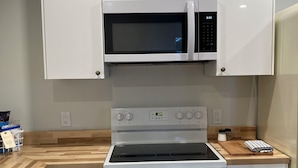 Une cuisine moderne avec des meubles blancs, un four à micro-ondes encastré, une cuisinière et un plan de travail équipé d’une planche à découper et d’ustensiles de cuisine.