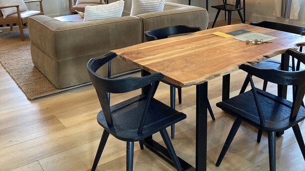 Un salon moderne avec un canapé, une table à manger en bois et des chaises noires. Un téléviseur à écran plat est fixé au mur, et une lampe se trouve sur une table d’appoint.