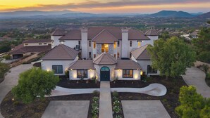 A large, multi-story house with a central entrance, surrounded by landscaped gardens and a driveway. - Hilltop Estate w/ Tennis Court, Pool, Sauna, Game Room, Theater, Panoramic Views (Temecula)