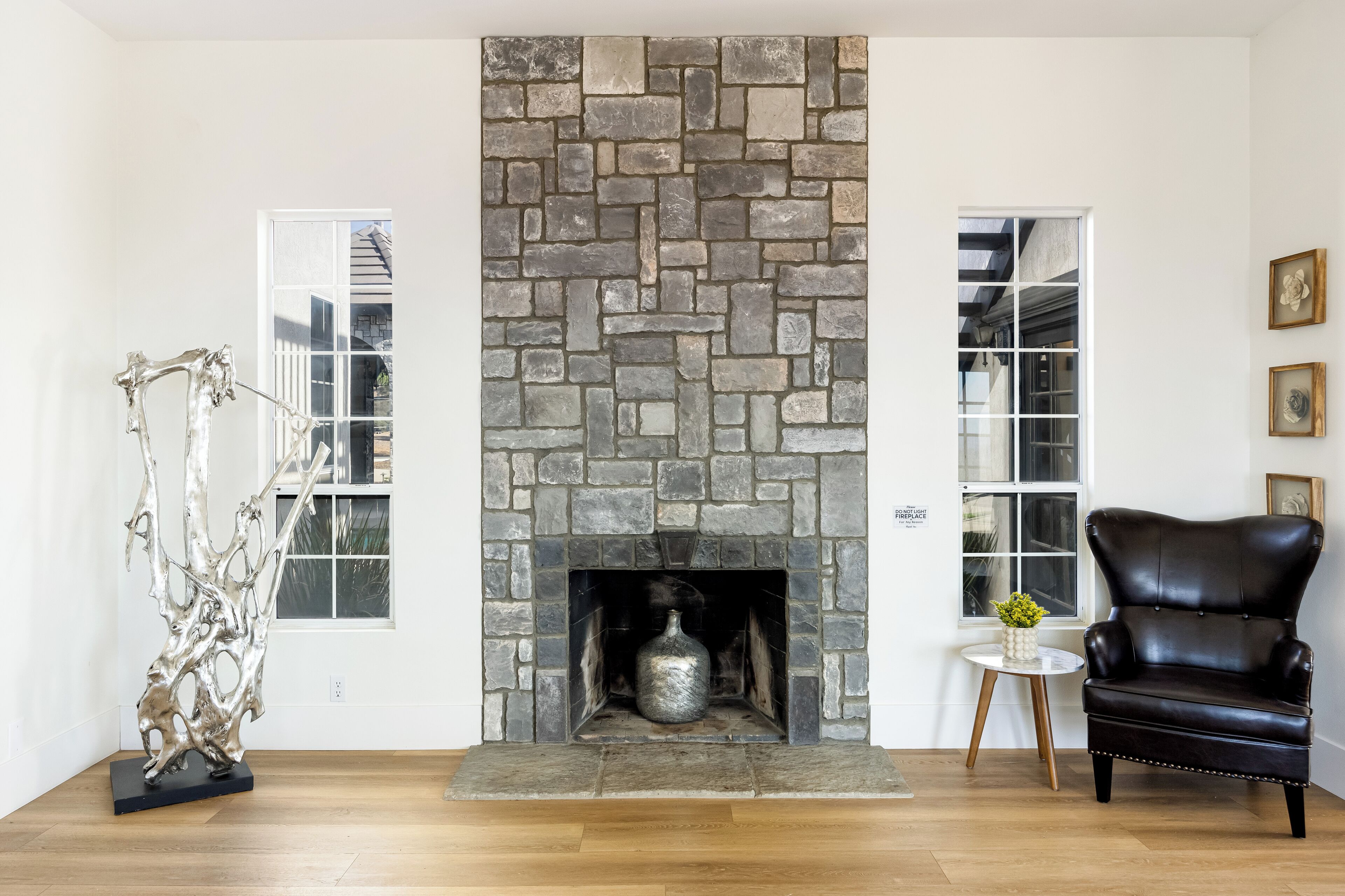 A room with a stone fireplace, a black leather chair, and a small table with a vase.