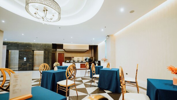 A dining area with tables, chairs, a chandelier, and a kitchen in the background. - Hotel La Vista (San Jose del Monte)