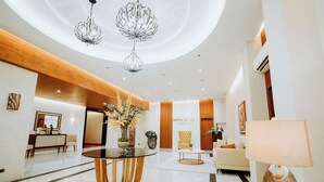 A modern hotel lobby with a round table, a sofa, a chandelier, and a wall-mounted sign. - Hotel La Vista (San Jose del Monte)
