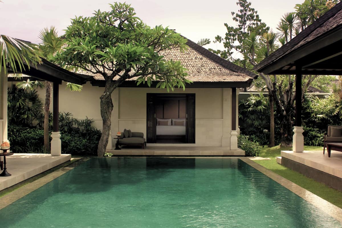 A poolside villa with a private bedroom, a covered outdoor seating area, and lush greenery.