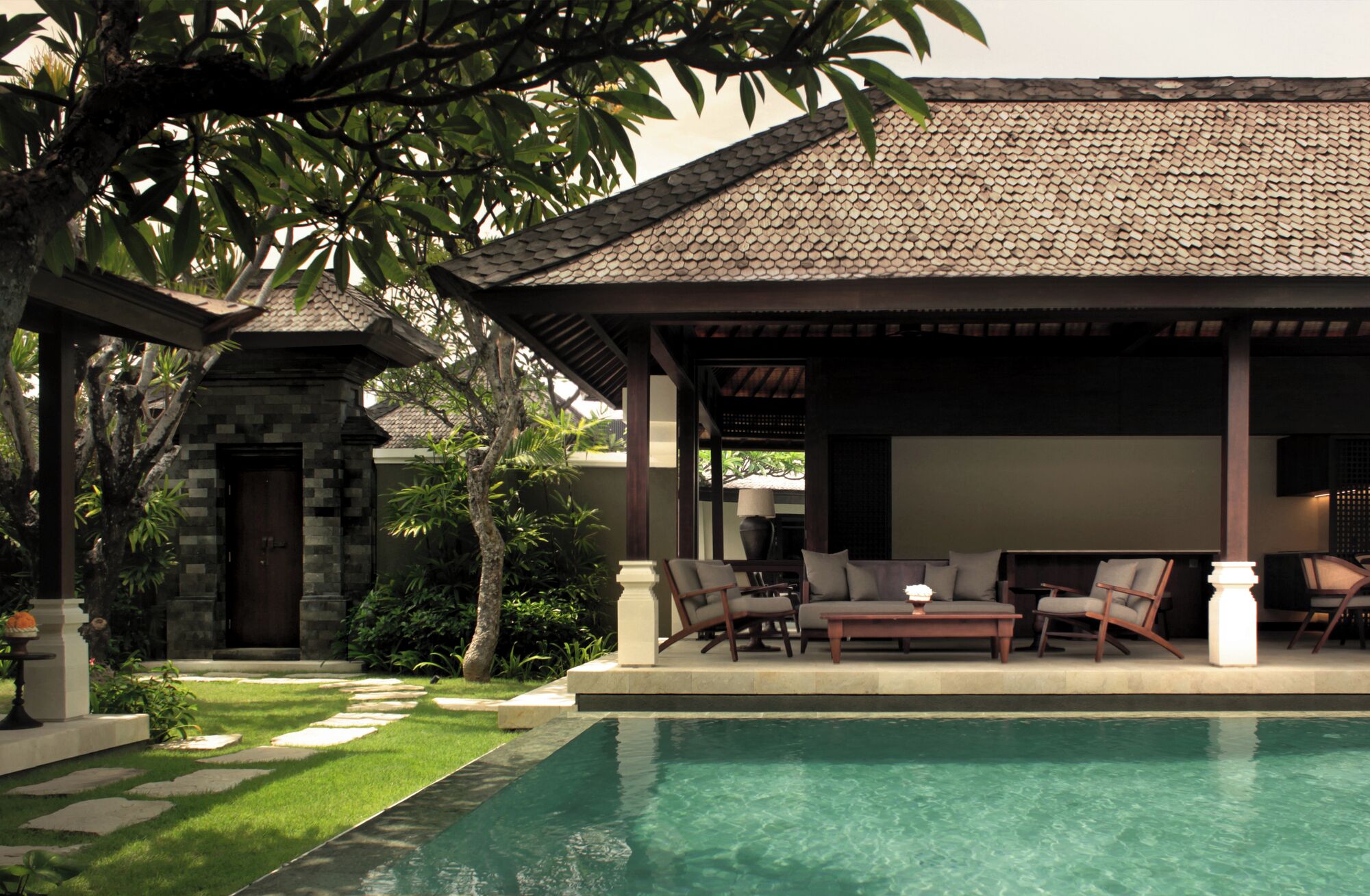 A poolside area with a covered seating area, stone pathway, and lush greenery.