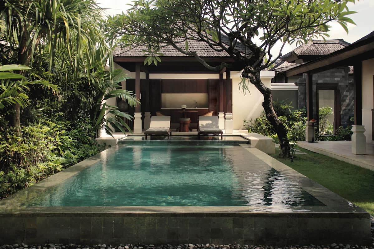 A rectangular pool with a stone edge, surrounded by lush greenery and a wooden deck.