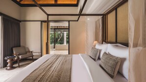 A spacious bedroom with a large bed, a chair, and a view of a garden through an open door. - Taman Estate by Ekosistem (Seminyak)