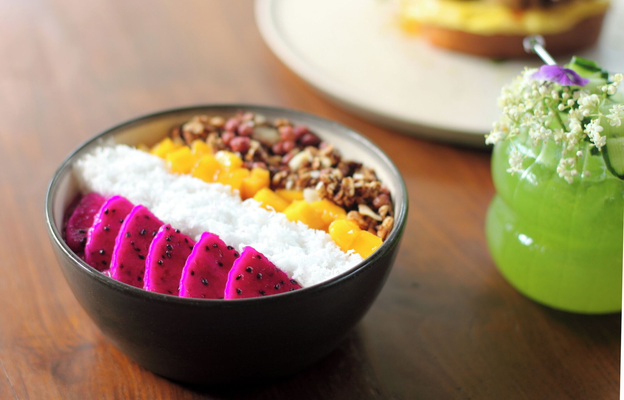 Un bol de dessert contenant du fruit du dragon, de la mangue et du granola, posé sur une table en bois.