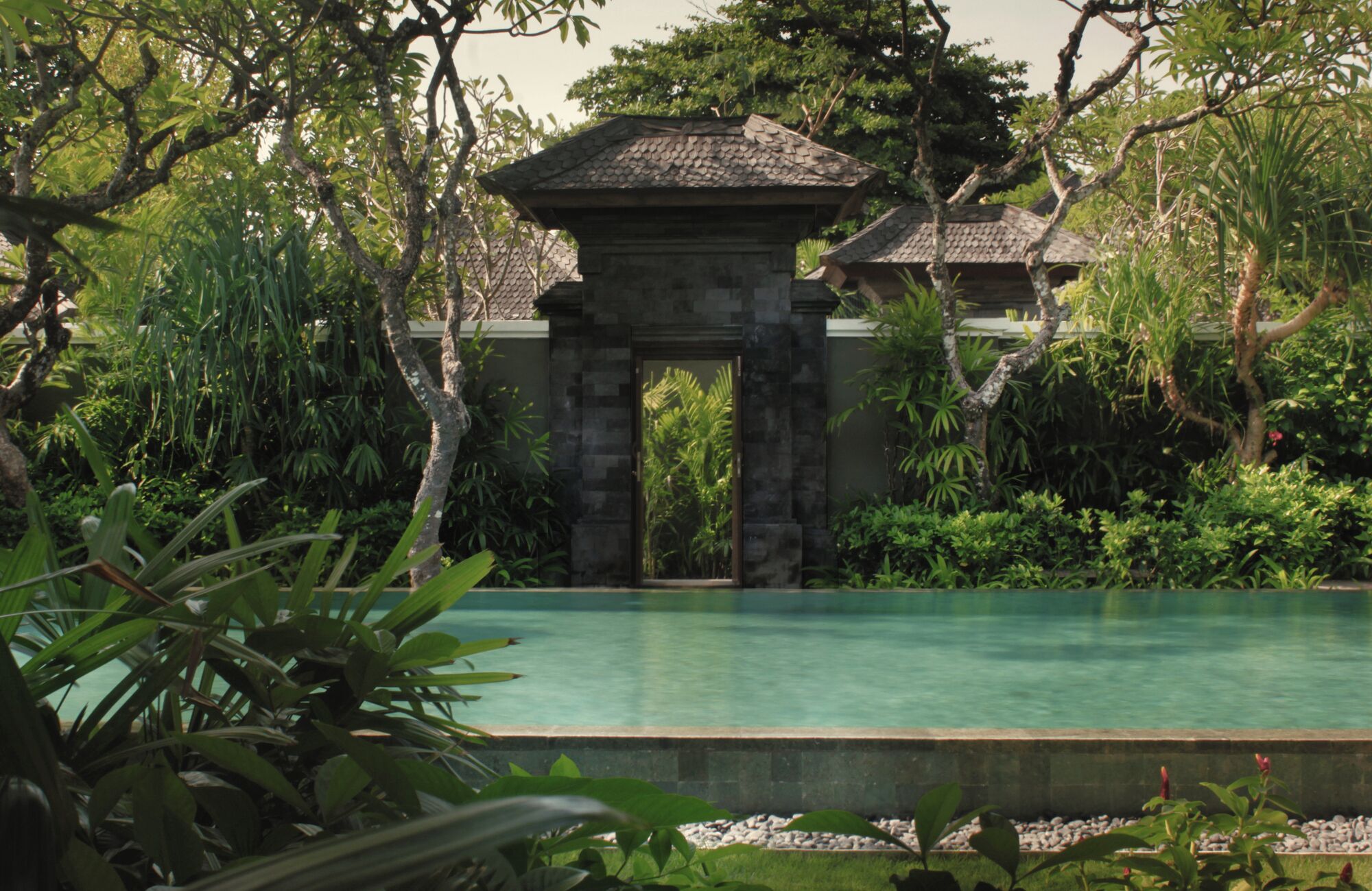 A stone archway leading to a pool surrounded by lush greenery.