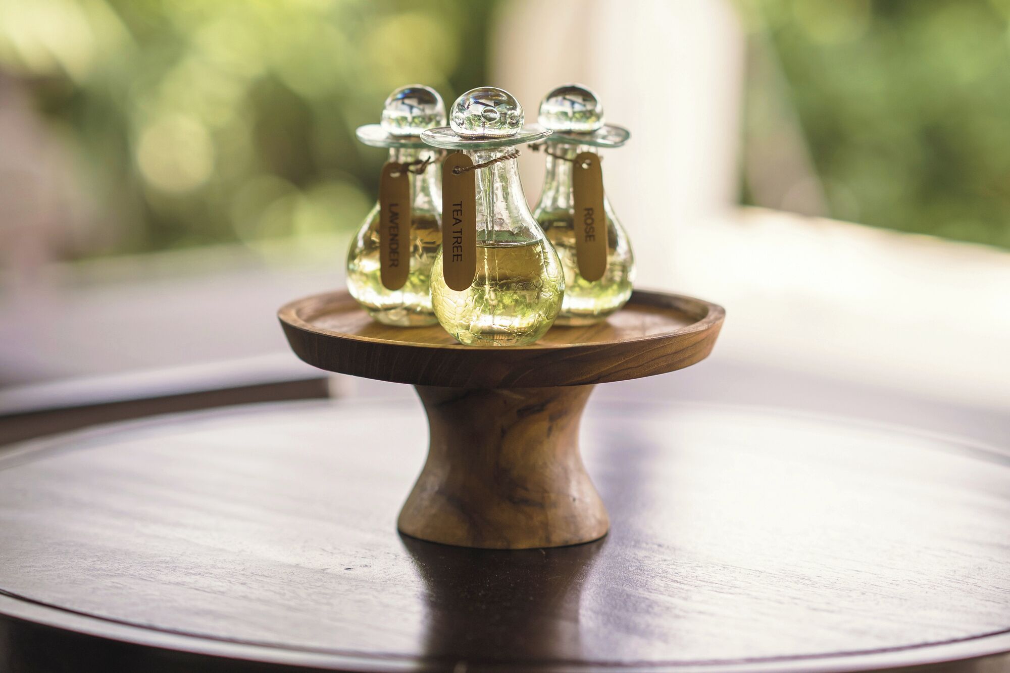 Un présentoir en bois supportant trois bouteilles en verre, chacune portant une étiquette, est placé sur une table ronde.