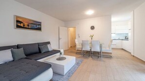 Ett modernt vardagsrum med en grå soffa, ett vitt soffbord och en matplats med ett vitt bord och stolar.