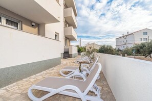 A row of white sun loungers on a stone patio with a white building in the background. - Starhouse 4 (Novalja)