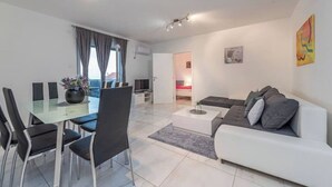 Ein modernes Wohnzimmer mit einem Glastisch, schwarzen Stühlen, einem weißen Sofa und einem Fernseher.