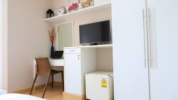 A compact room with a desk, chair, television, and a small refrigerator.