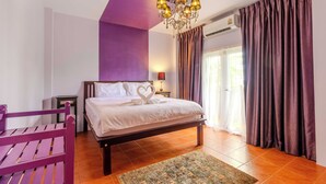 Un dormitorio con cama, pared morada, candelabro, ventana con cortinas y banco de madera.