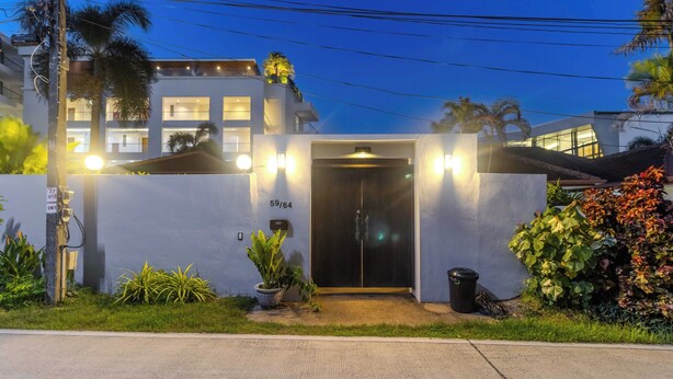 Un edificio moderno con una entrada bien iluminada, un cartel con el número visible y un pequeño jardín con plantas.