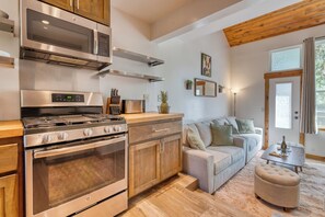 Eine moderne Küche mit Edelstahlgeräten, Holzschränken und einem gemütlichen Wohnbereich mit Sofa und Hocker.