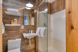 A bathroom with a wooden wall, a glass shower enclosure, a white sink, and a toilet. - 3 Mins to the Lake, Near Tahoe City! Modern Cabin w/ Deck Lounge | Dollar Hill (Tahoe City)