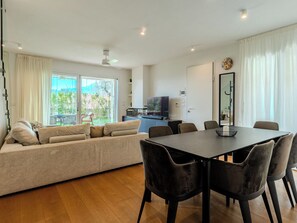 Un salon moderne comprenant un canapé, une table à manger, des chaises, un téléviseur et une vue sur l’extérieur.