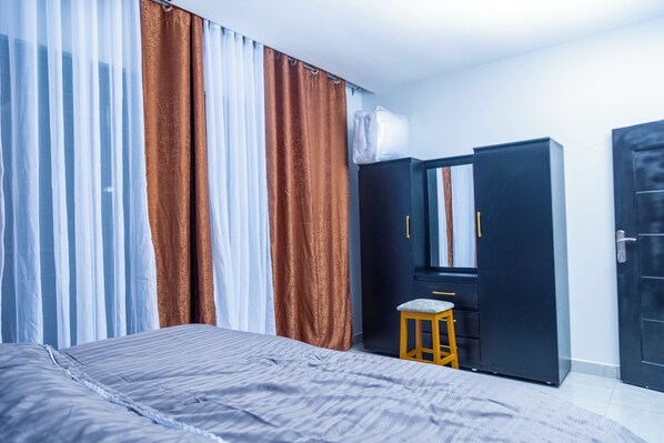 A bedroom with a bed, a small stool, a wardrobe, and a door.